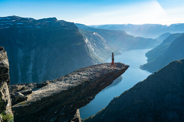Trolltunga, Norway. Man tourist doing acrobatic handstand on the top of mountain's cliff edge named...