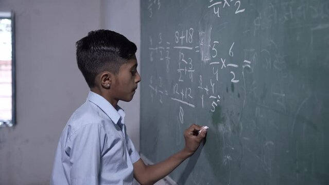 Rural indian student write solve math sum on chalkboard or blackboard in classroom, Intelligent schoolboy studying, Education, Knowledge.