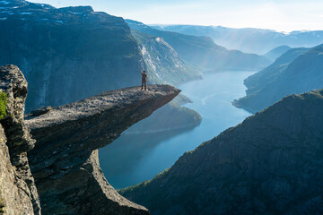 Trolltunga, Norway. Happy man tourist on the top of mountain's cliff edge named Trolltunga raising...