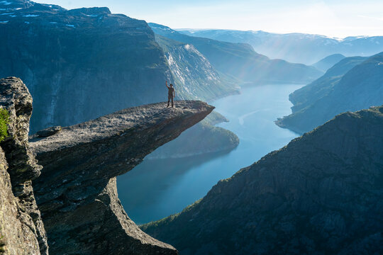 Trolltunga, Norway. Happy man tourist on the top of mountain's cliff edge named Trolltunga raising his hands up and watching Norwegian mountains. Adventure travel lifestyle emotional spectacular view.