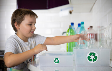 A child participates in sorting plastic in the kitchen to be sent for recycling. Cute boy child...