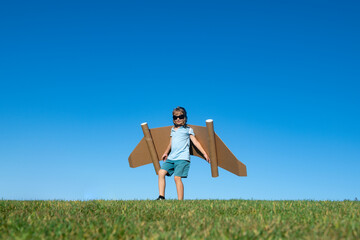 Child playing outside on green grass and blue sky. Kid pilot with toy jetpack. Kid boy play with...