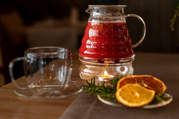 Inviting author berry tea in a glass pot, warmed by a candle, with a clear cup and citrus accents offering a cozy vibe.