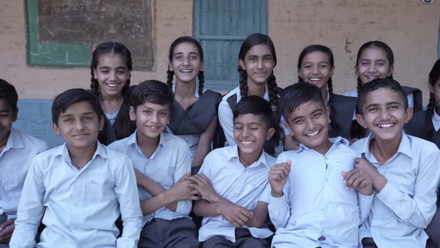 Education, Group of happy rural indian school students sitting together looking at camera, India. Slow motion shot.