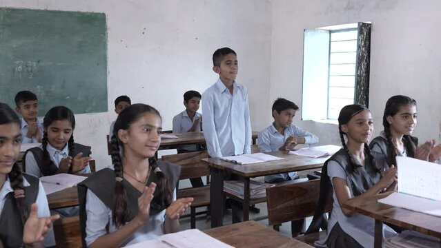 Indian students clapping for intelligent schoolboy at classroom, Children give applause for brilliant boy. Rural india.