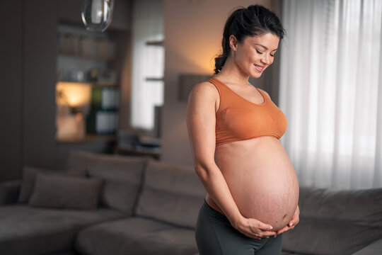 A beautiful pregnant woman holding her stomach while doing relaxing exercises at home