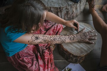 Woman seated, applying intricate henna designs to her arms