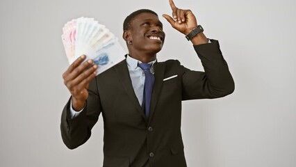Smart african american man in suit, finger pointing up with excited expression, holding chinese yuan banknotes, number one question in mind on white isolated background, he's got a happy money idea!