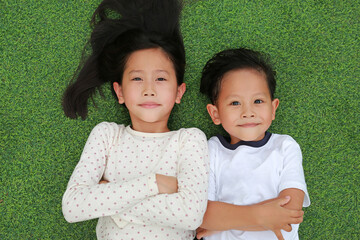 Asian little child boy and girl lying on green grass outdoors in summer park. Portrait of sister and brother resting in garden happy smiling together. Above view - 793792827