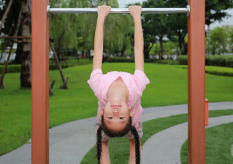 Asian girl child enjoy to hanging upside down on aluminum fence in public park.