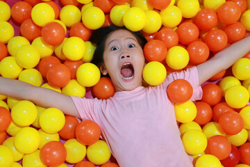 Excited Asian young girl while playing at colorful plastic balls playground. - 793794084