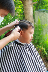 Portrait of Asian boy cut in hairdresser's machine in the garden - 793794448