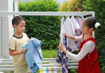 Asian girl child and little boy helping to do dry the clothes at the garden near house. Sister and little brother are help to housework. Kids hanging the laundry on a clothesline rail. - 793794895
