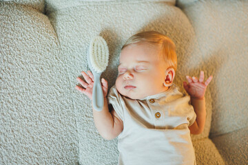 A small baby is sleeping on the couch. Baby in T-shirt and pants with closed eyes.