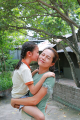 Happy family Asian girl child kiss on the cheek her mother while in the nature garden. Mother carrying daughter. - 793795211