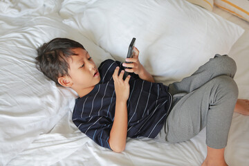 Portrait of Asian little boy playing a smartphone while lying on bed at morning.