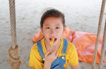 Close up of Asian girl eating French fries with dip cheese while sitting on swing at the beach.