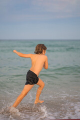Kid running and splashing in the sea. Summer vacation. Child Running Along the beach. Active little kid running along sea beach during leisure sport activity. Sporty kid running in nature.