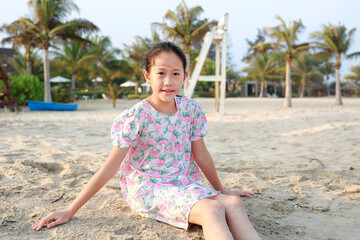Smiling Asian young girl child relax on beach sand and looking camera at summer holiday. - 793797013