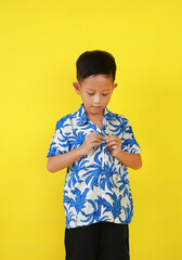 Portrait of Asian boy child buttoning up their own shirt isolated on yellow studio background. - 793797087