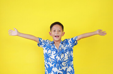 Portrait of happy Asian boy child in summer dress costumes raised arms or open hands wide gesture isolated on yellow background.
