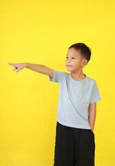 Portrait of Asian little boy child pointing index finger or forefinger and looking beside while standing isolated on yellow background.