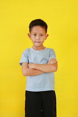 Portrait of smiling Asian boy age about 7 years old standing and cross arms over chest looking straight at camera isolated on yellow studio background. - 793797433