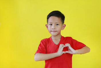 Portrait of happy Asian boy with a heart shape symbol with hands isolated on yellow background. - 793797615