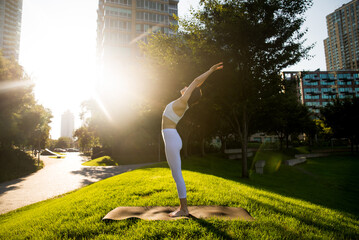 Woman doing yoga in a park - Sportive female adult doing meditation and gymnastic morning routine at the city park