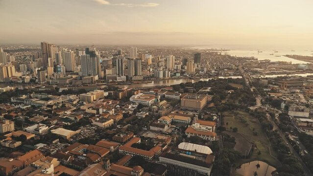 Sunset harbour city with ships, yachts at ocean bay aerial. Modern skyscrapers, cottages and houses at sun set light cityscape. Cinematic Philippines metropolis of Manila downtown drone shot