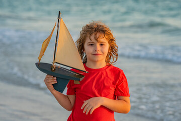 Child playing with a toy boat. Little kid boy sailing toy ship on sea water. Summer vacation with kids. Kid dreaming about sailing. Concept of childhood and family vacation. Travel with children.