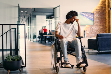Fototapeta na wymiar A African-American teenager in a wheelchair sits sadly amidst the bustling backdrop of a modern startup office, surrounded by his business colleagues.