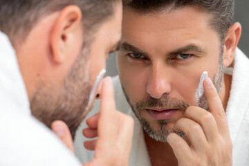Man applying face cream. Beauty routine. Man with perfect skin. Anti-aging and wrinkle cream. Concept of male beauty. Close up face of man applying cream to skin. Skincare and cosmetics concept.