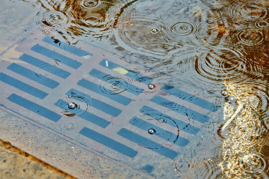 Large puddle due to clogged storm drain. Flooding across road during rain, blocked street drain. Plumbing problems in the city, clogged drain, water flooding. Selective focus