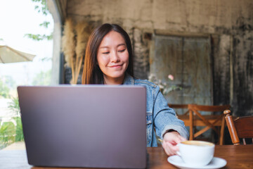 Portrait image of a young woman drinking coffee while working on laptop computer in cafe - 793812471