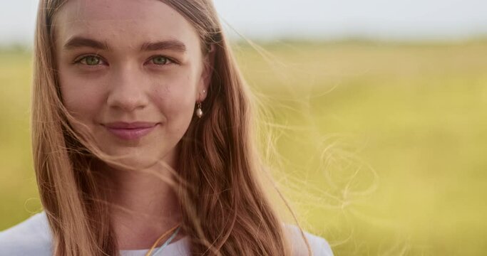 Close up portrait of young girl turning her head, looking at camera. Non urban scene, windy day, yellow field, candid child smilng, natural beauty, ukrainian teenager. High quality 4k footage