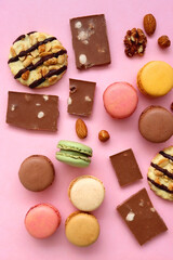 Pastel macarons, almond chocolate, peanut butter cookies and various nuts on bright pink background. Top view.