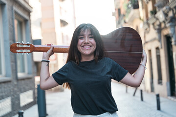 portrait of a woman smiling and looking at the camera with an acoustic guitar on her shoulders