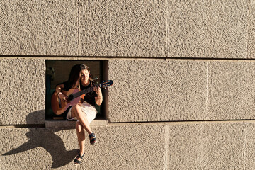 full view of a woman sitting in a wall recess playing the guitar with copy space for text....