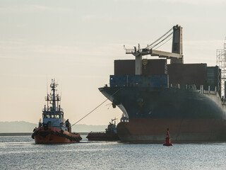 Tugboat assisting a large cargo ship near the port during early morning hours, with a buoy in the...