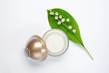 Sierkussen Jar of cream and lily-of-the-valley flowers on white background. Cosmetic products. Top view, flat lay. © Photo