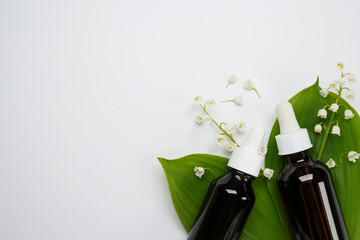 Bottles with essential oil and lily-of-the-valley flowers on a white background. Top view, flat...