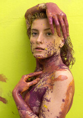 Portrait of a young artistically abstract woman in pink and yellow painted against light green wall background