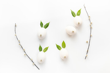 Creative layout with white eggs and green leaves in the shape of bunnies and willow branches