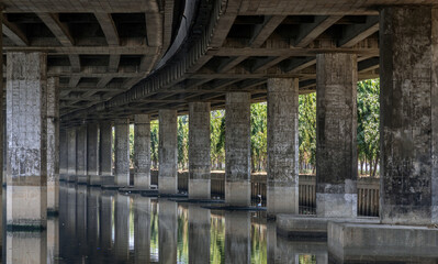 Perspective view of concrete pillars under Khlong Toei Expressway, with calm surface water...