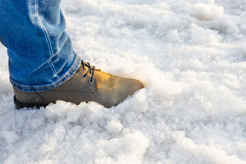 a man in boots walks through melted snow.