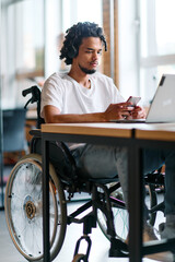 An African American businessman in a wheelchair takes a work break, using his smartphone while...