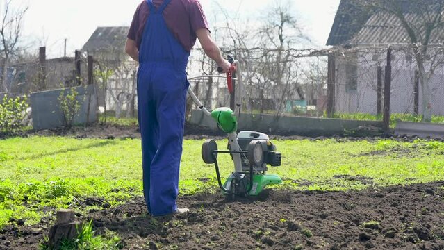 A farmer in the garden tills the land with a motorized cultivator or power tiller, preparing the soil for planting crops