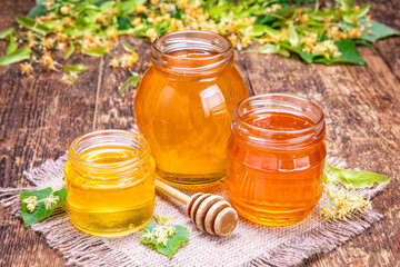 Three jars of honey are on a table with a honeycomb and a honey stick
