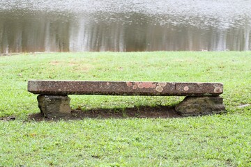 a bench made of a stone slab at the edge of a water body in a park